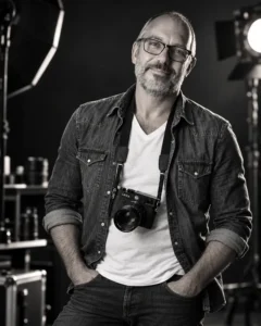 Luca Cavazzuti, fotografo, in studio con una macchina fotografica al collo, in bianco e nero