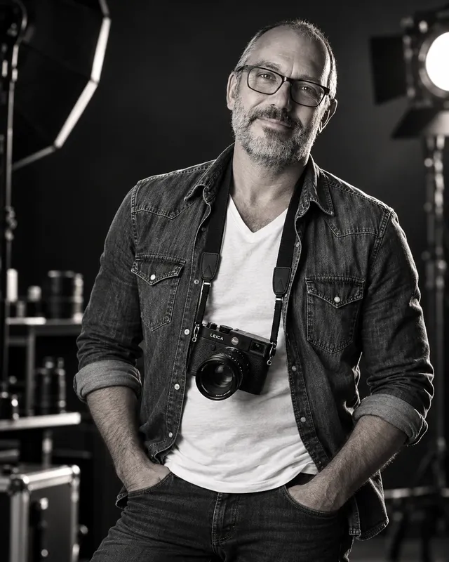 Luca Cavazzuti, fotografo, in studio con una macchina fotografica al collo, in bianco e nero
